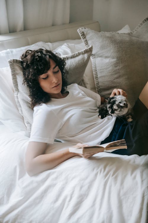 Free Calm woman reading book and caressing cat on bed Stock Photo